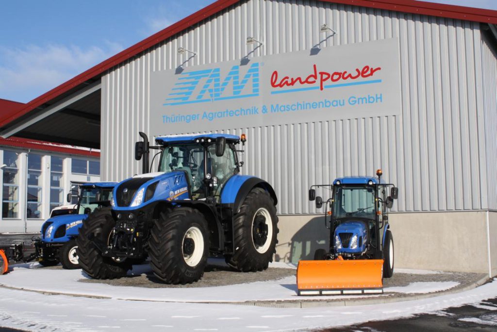 Traktor und weitere Landmaschinen vor einer Produktionshalle der Firma TAM