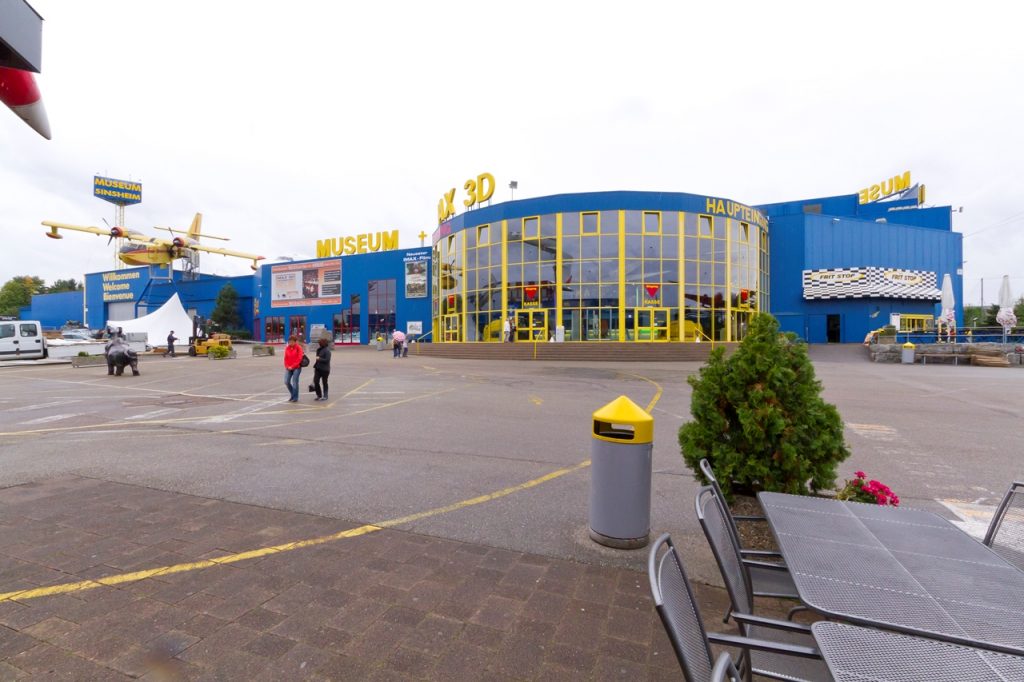 Moderne Museumsfassade mit gelben Glasfronten und aufgehängtem Flugzeugmodell im Außenbereich