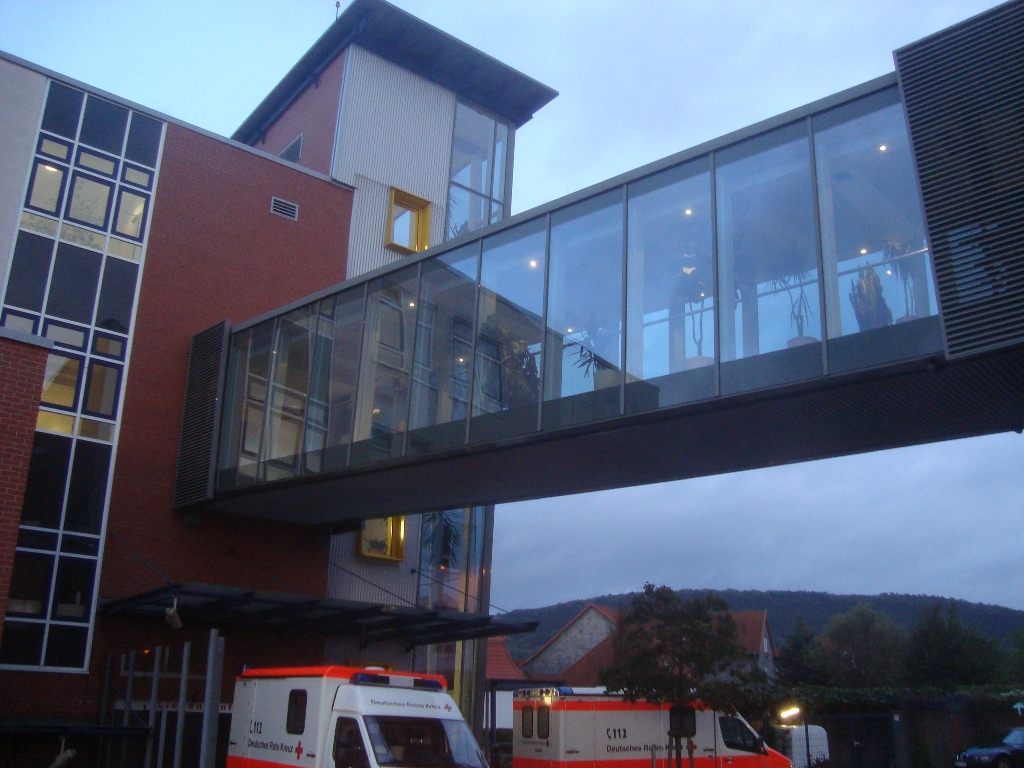 Verbindungssteg aus Glas zwischen zwei Klinikgebäuden mit Blick auf die umliegende Landschaft