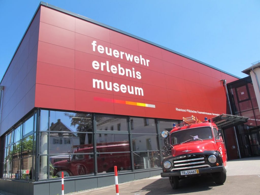 Außenaufnahme des Feuerwehr-Erlebnismuseums Hermeskeil mit roter Fassade und historischem Feuerwehrfahrzeug davor