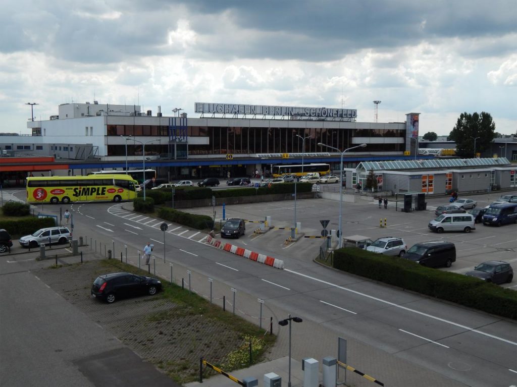 Flughafengebäude mit Vorfahrt, parkenden Autos und Bussen auf dem Vorfeld an einem bewölkten Tag