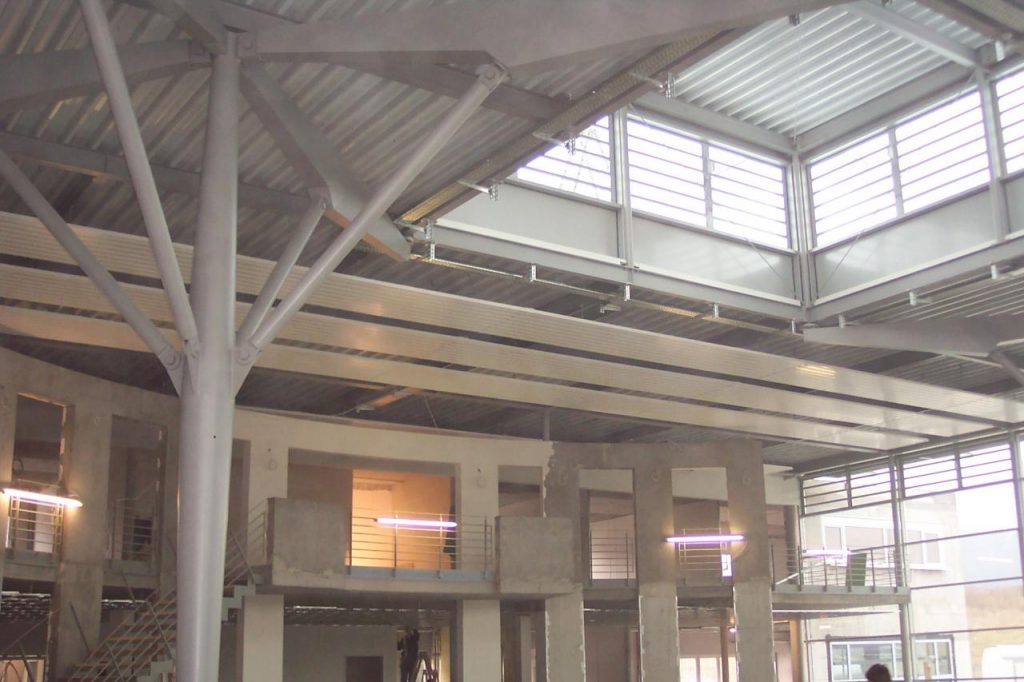 Angebrachte lange Sunline Deckenstrahlplatten in einer hellen Industriehalle mit Oberlichtern und Sichtbeton