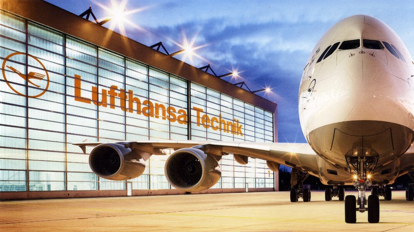 Flugzeug vor der Wartungshalle von Lufthansa Technik mit beleuchteter Glasfassade im Hintergrund