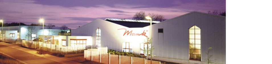 Beleuchtetes Firmengebäude der Mank GmbH in Dernbach am Abend mit moderner Fassade und Unternehmens Schriftzug